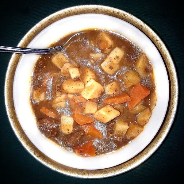 A bowl of beef stew with tender chunks of beef, potato and carrot in a thick brown sauce.