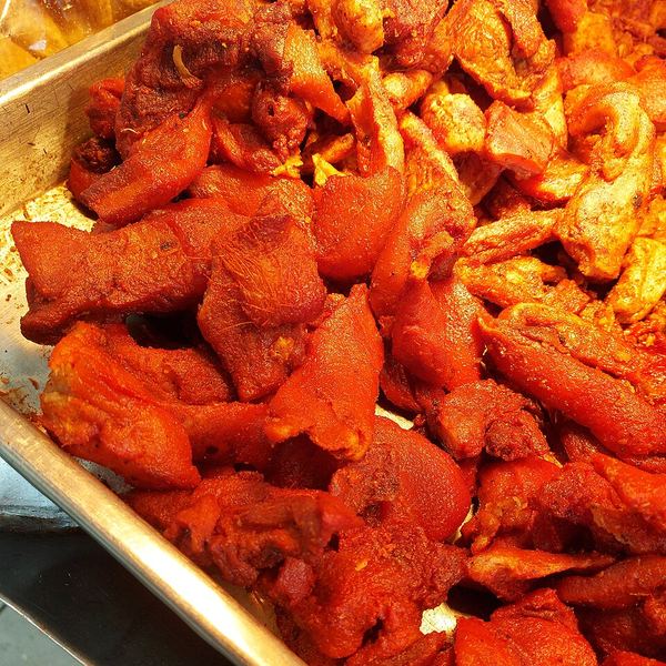 A large metal tray of carnitas, the pork deeply browned and glistening, cut into rough pieces.