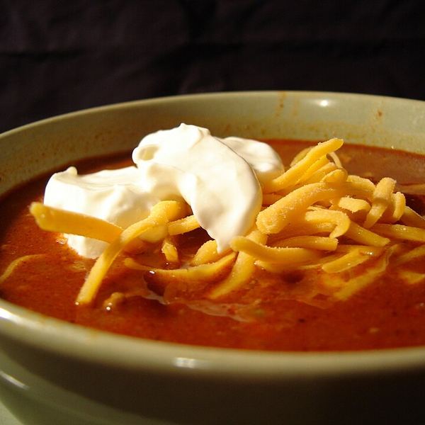 A bowl of thick chili topped with sour cream and cheese, the sauce clearly coating rather than pooling.