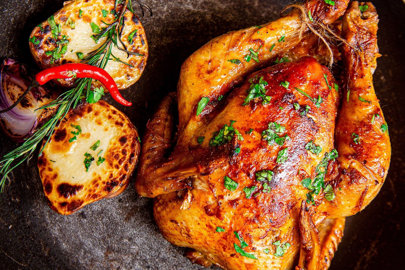 A whole roast chicken with browned skin in a roasting pan.